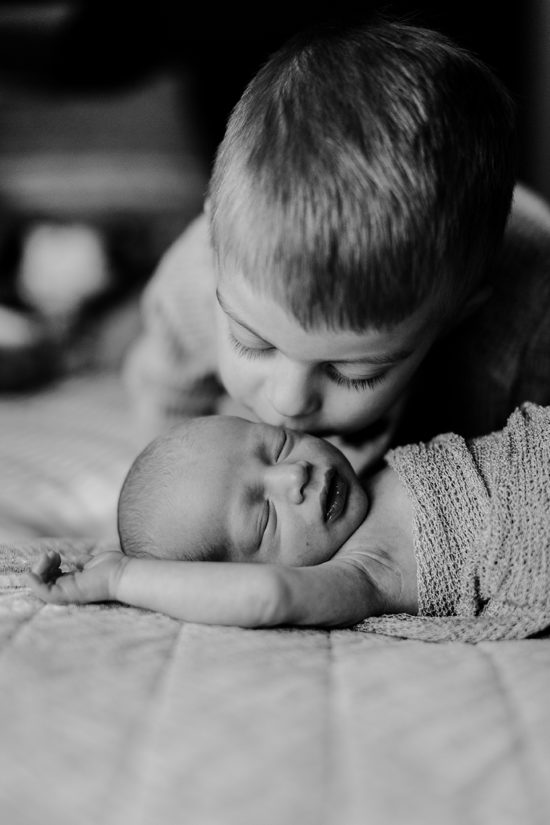 Big brother kisses baby during a newborn photography session