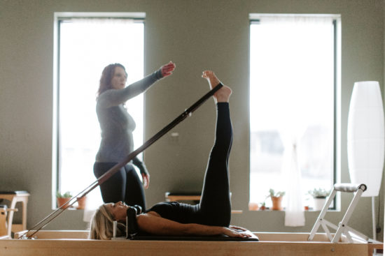 Woman instructs pilates student as she stretches for a branding photography session