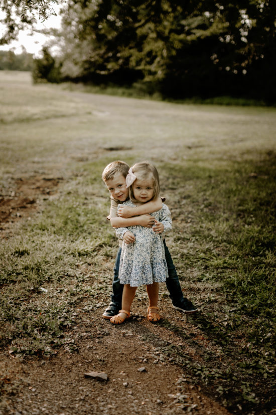 Brother hugs his sister while the two kids look at the camera for family photos.