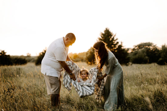 Couple holds their toddler in a blanket and rocks her during their photo shoot