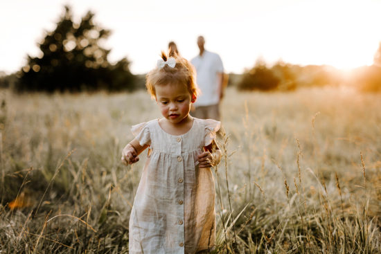 Toddler walks through a field, away from her mom and dad during their family photo session