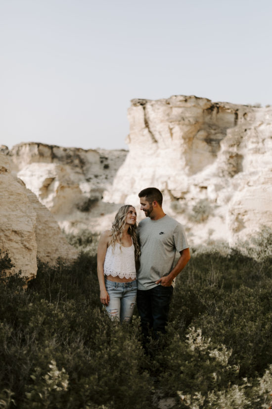 Couple smiles at each other and embrace, Kansas rock formations are in the background