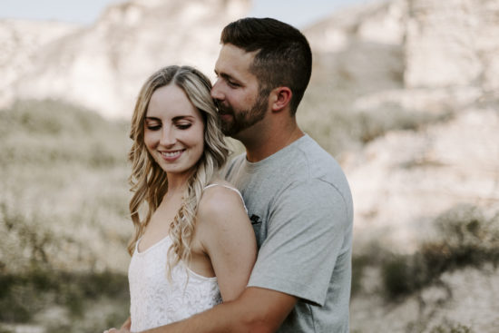 Man whispers into his fiancée's ear with Little Jerusalem Badlands in the background