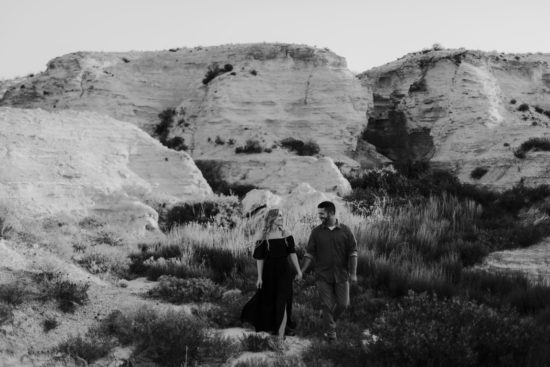 Couple holds hands and smiles at each other with Little Jerusalem badlands in the background for their Kansas engagement photos
