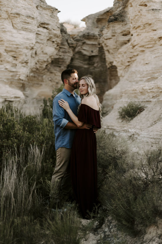 Man and woman embrace each other with limestone rock formations in the background for their Kansas engagement photos