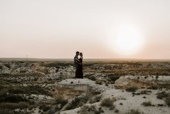 Couple standing on a Little Jerusalem limestone bluff embrace each other with the sun setting in the background