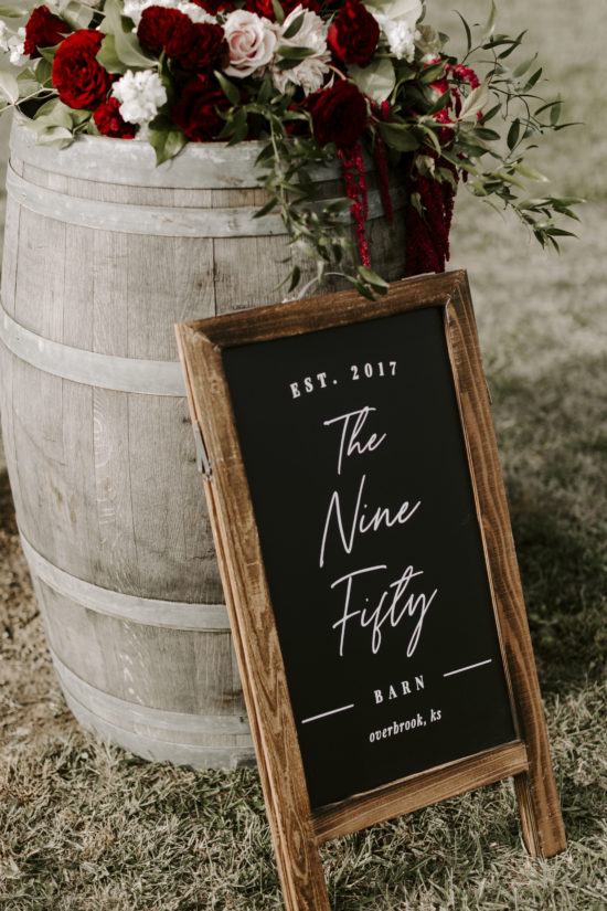 A barrel props up a chalkboard that reads "The Nine Fifty barn" — the location of this Kansas farm wedding