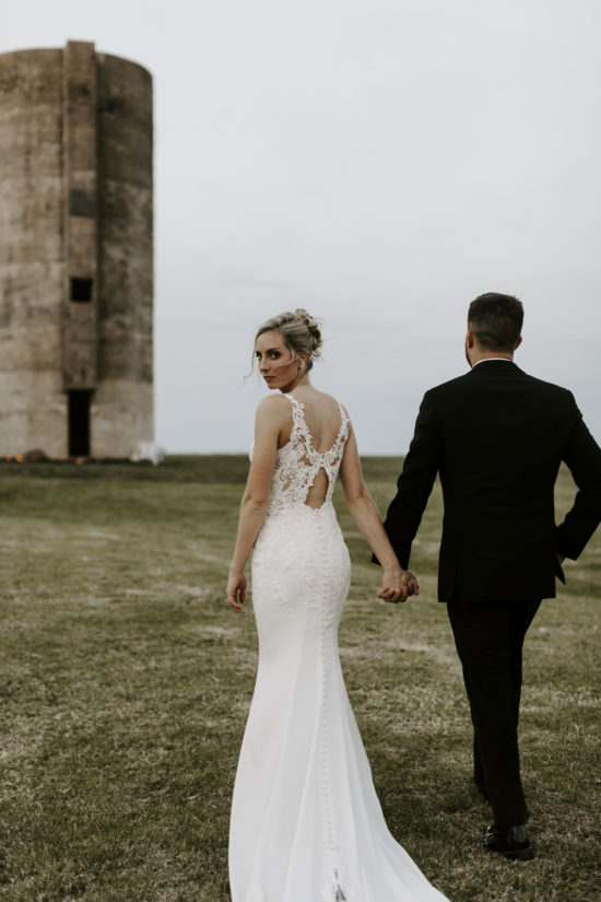 Groom walks toward the silo on his Kansas farm while the bride looks back at the camera