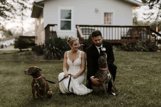 Bride and groom crouch with their dogs at their Kansas farm wedding