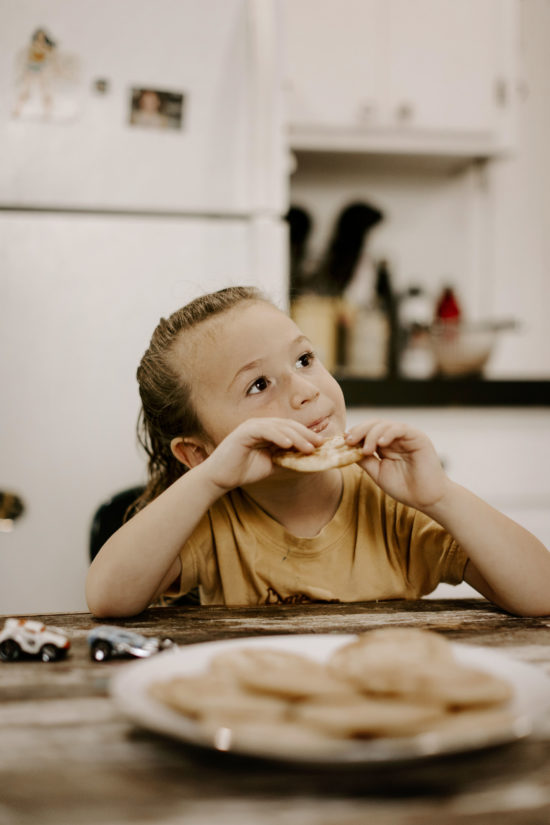 Child sits at a table eating a cookie while taking lifestyle photos
