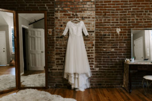 The Bride's dress hangs against a brick wall before the couple's Abe and Jake's wedding