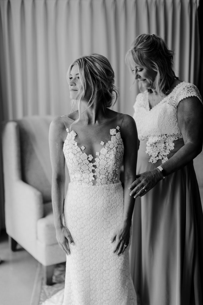 The bride's mother-in-law helps bride zip up her dress before the wedding
