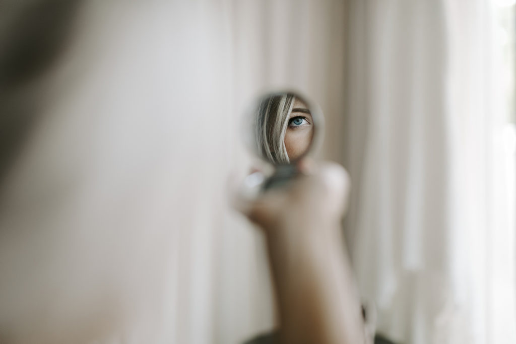A bride looks into a small hand mirror before her wedding 