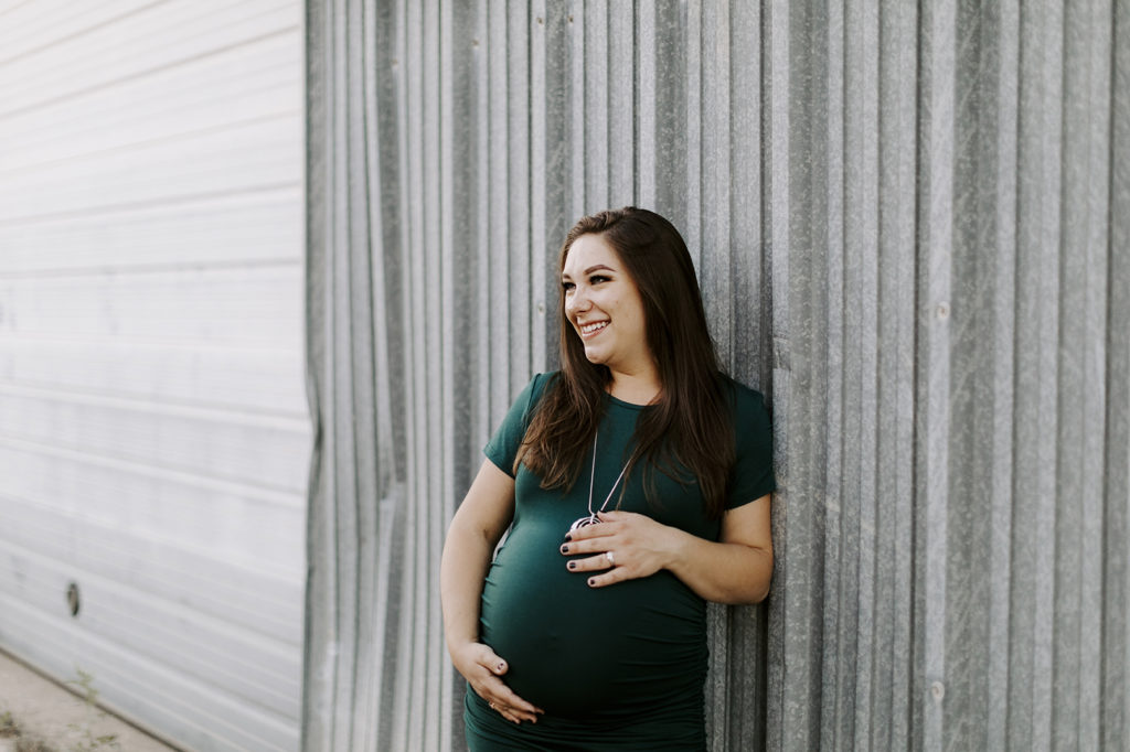 A pregnant brunette woman holds her belly and smiles during her maternity session.