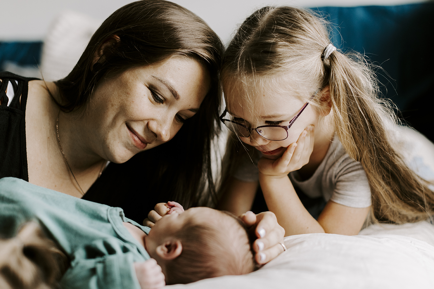 A mom and big sister gaze at their new baby during their newborn session