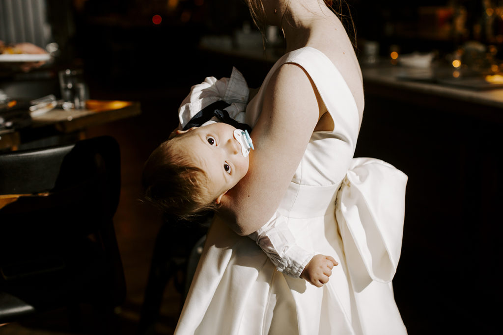 The bride holds their baby while he looks at the camera.