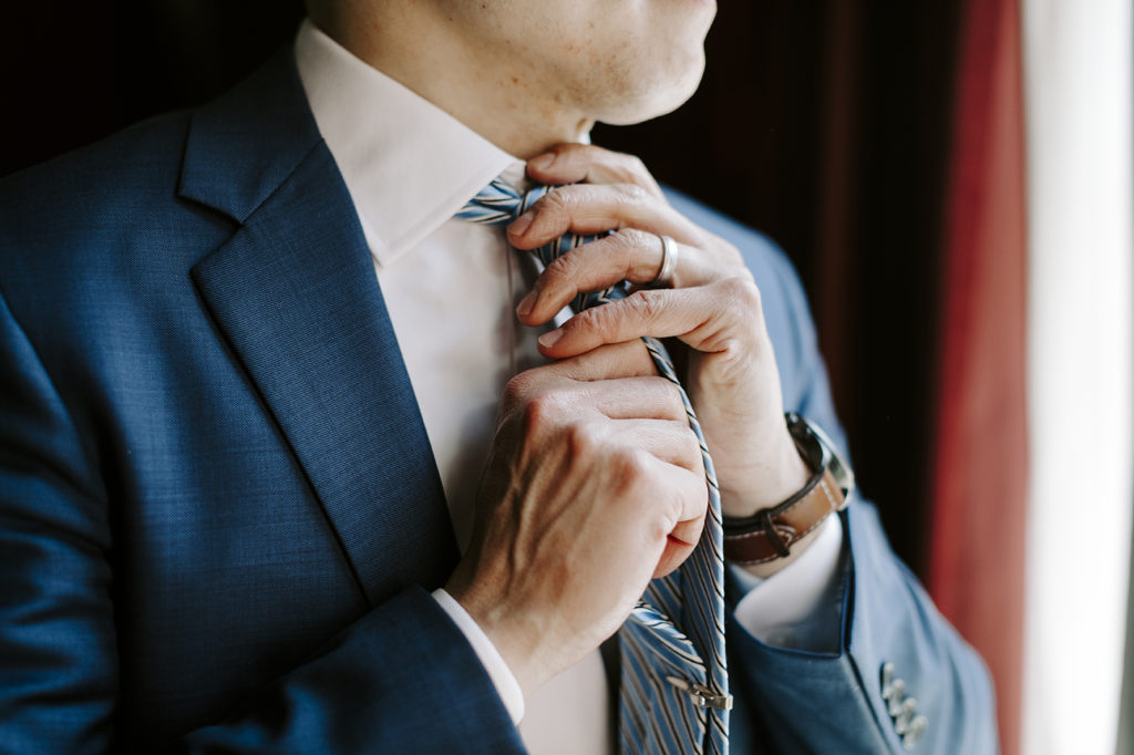 The groom arranges his tie before his upscale Kansas City wedding.