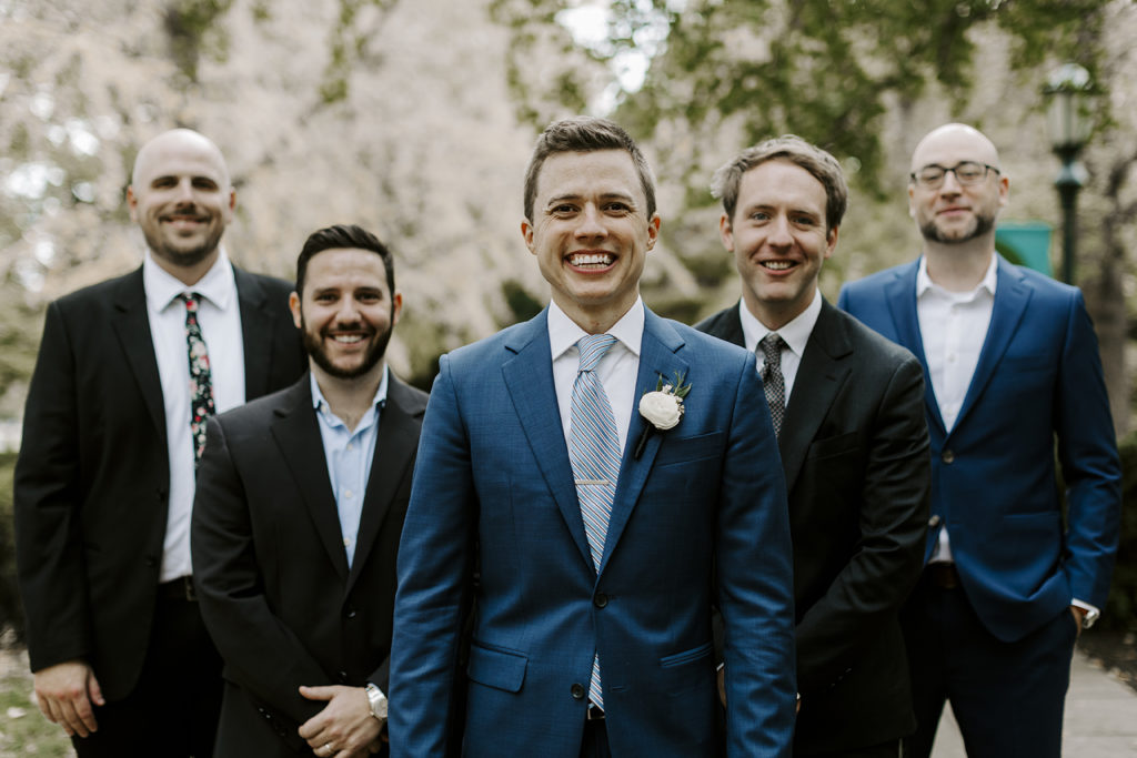 The groomsmen line up behind the groom and smile at the camera.