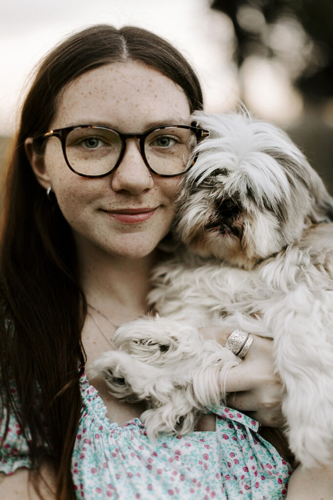 A woman in glasses holds her Shih Tzu up next to her face during their Lawrence pet photo session.