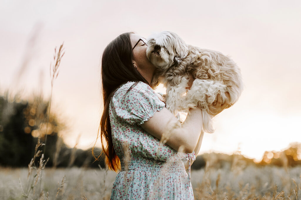 A woman holds her Shih Tzu up in the air and kisses the dog during their Lawrence pet photo session.