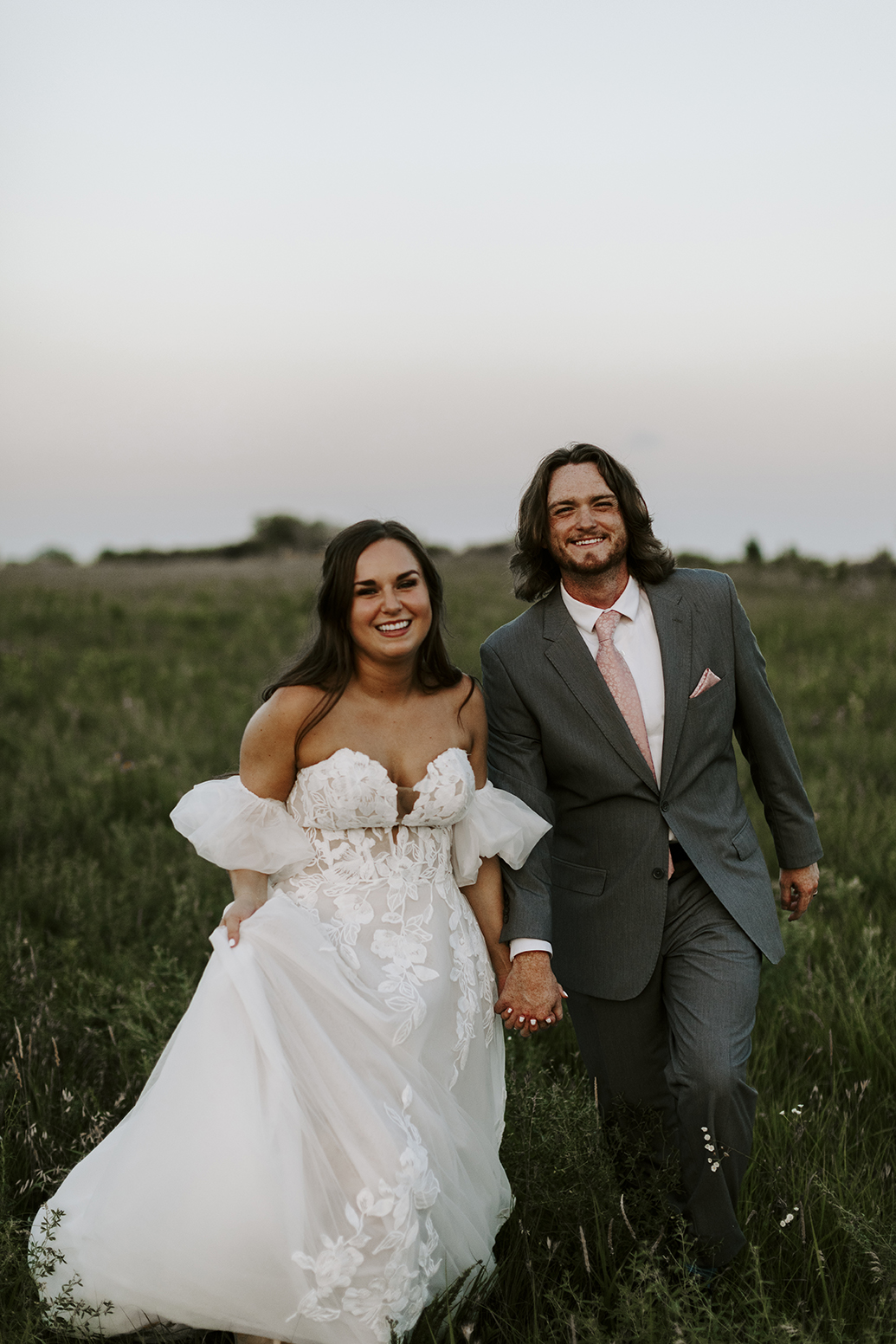 Katie and Trace hold hands and smile at the camera during their Kansas lakehouse wedding.