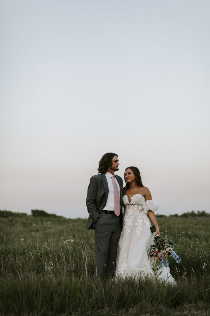 The bride and groom pose in a field after their Kansas lake house wedding.