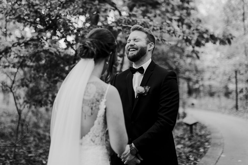 The groom laughs with his eyes closed while holding his bride's hands.