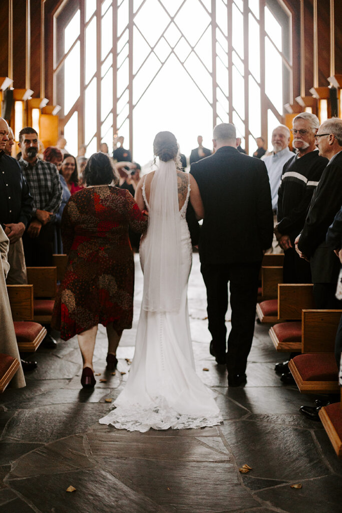 The bride and her parents walk down the aisle of Marjorie Powell Allen Chapel at her Powell Gardens wedding.