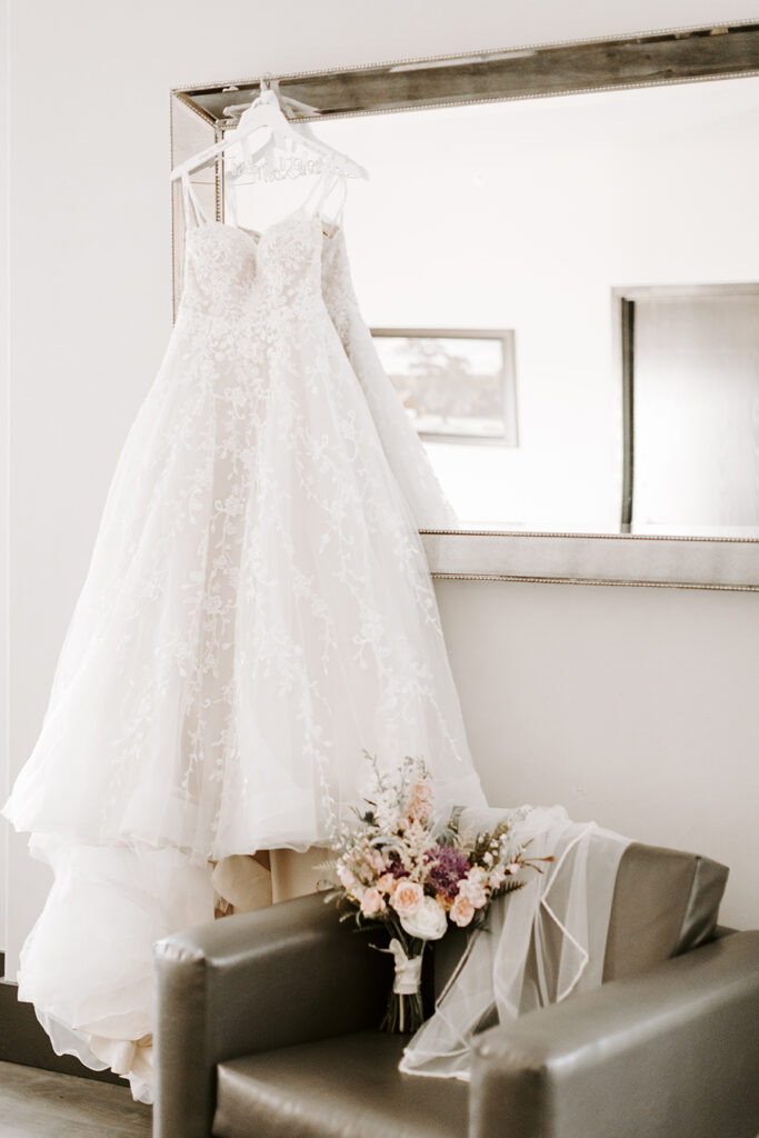 A wedding dress hangs from the mirror in a room during Michelle and Sailor's Oread wedding in Lawrence KS.