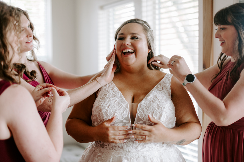 A bride smiles while her friends fawn over her ahead of her North Lawrence wedding